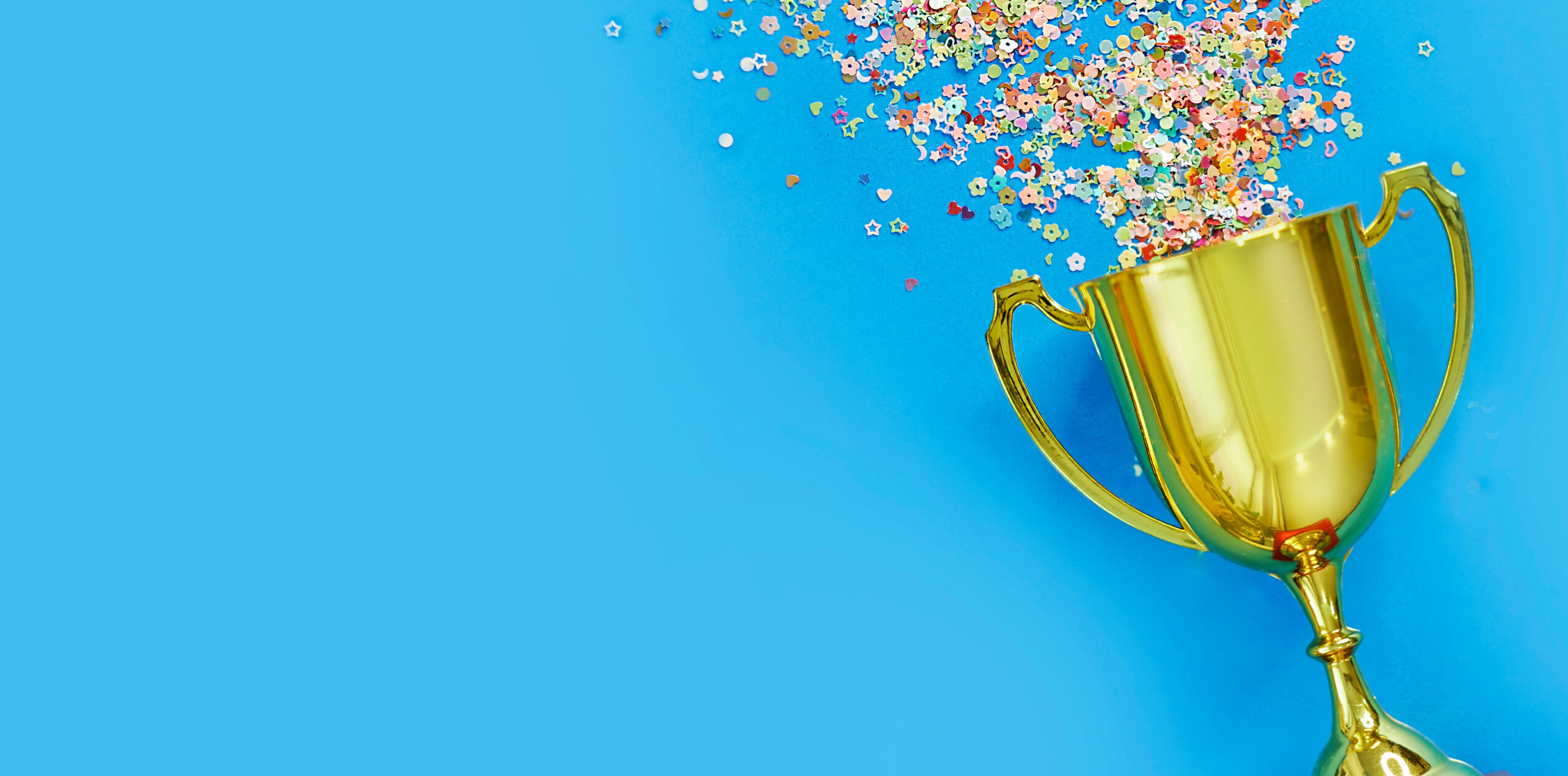 Golden trophy cup with confetti spilling out of it on a blue background.